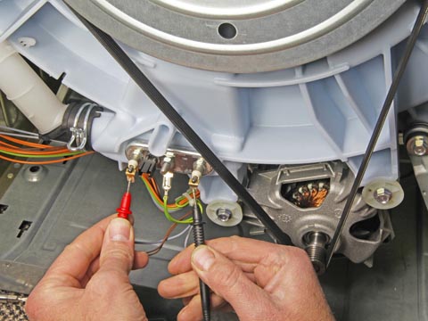 Close up of washing machine technician's hands while test the heater element at the back of a washing machine